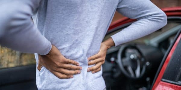 Man holding his back in pain with both hands outside car