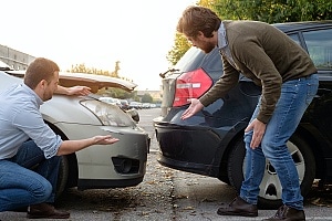 two men looking at the damage from their car accident