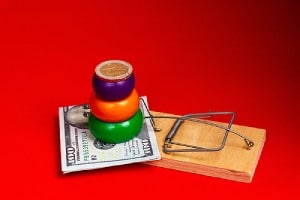 Dollar bill and pyramid with coins stack upon a mousetrap. There are certain common signs of fake lottery scams